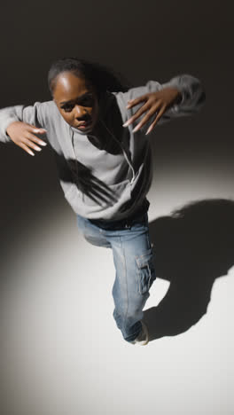 Vertical-Video-Full-Length-Studio-Shot-Of-Young-Woman-Wearing-Hoodie-Dancing-In-Spotlight-With-Shadow